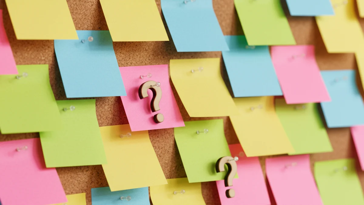 Mural de cortiça com post-its coloridos e pinos em formato de interrogação.