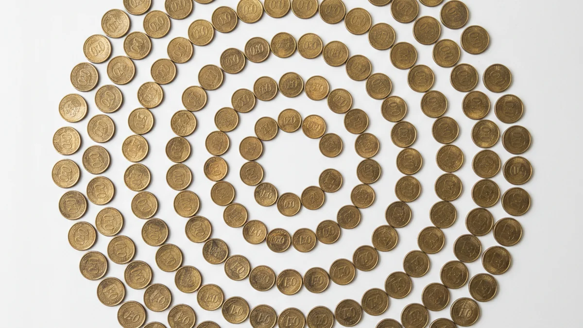 Moedas de real dispostas em espiral decrescente sobre superfície branca, vistas de cima.