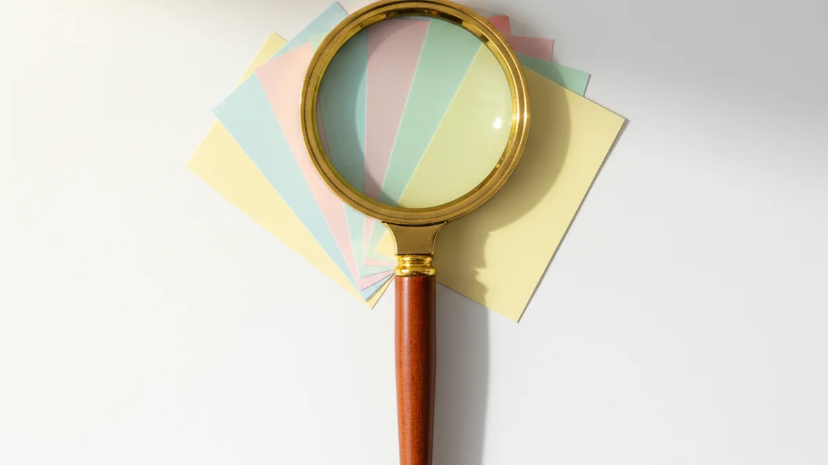 Lupa de latão sobre cartões coloridos em mesa de madeira iluminada por luz dourada.