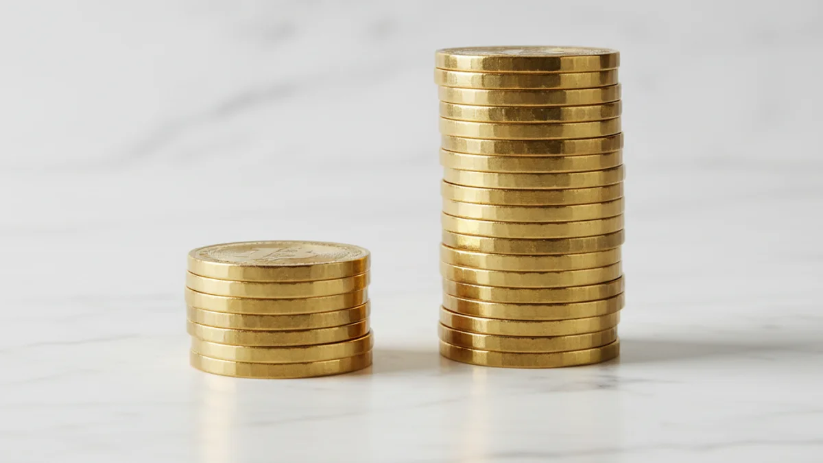 Duas pilhas de moedas douradas em proporção quatro para um sobre mármore branco.