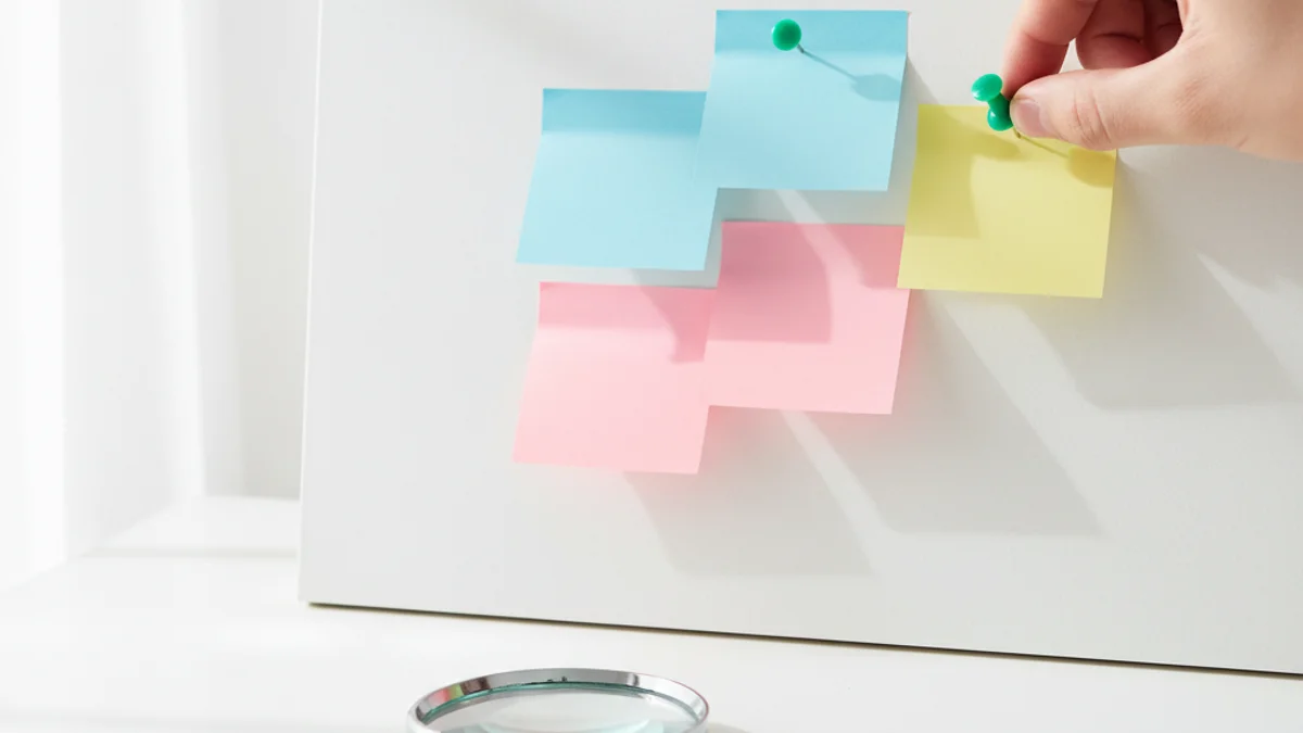 Mão colocando alfinete em quadro de cortiça com notas coloridas formando gráfico.
